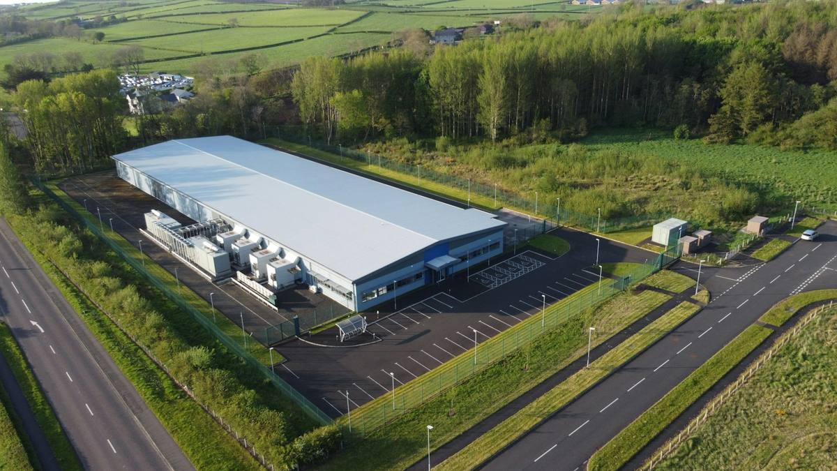 Aerial view of a data center building with its cooling plant alongside, car park and fenced grounds