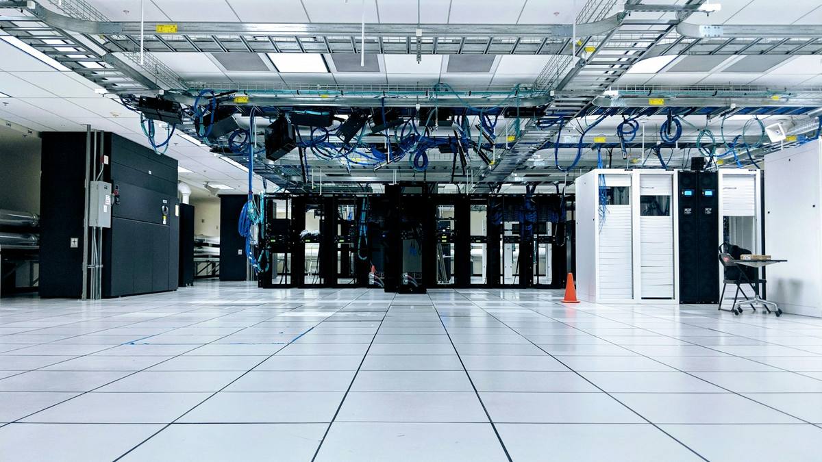 Inside a data hall with overhead cable trays, black server cabinets and a raised floor